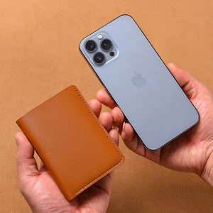 Slim brown leather card holder for women shown next to a smartphone for size comparison