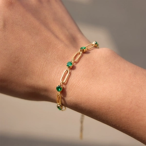 Macro view of gold paperclip chain bracelet with green emerald zircons on wrist