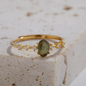 Macro shot of an adjustable gold ring with oval green gemstone on a textured stone base