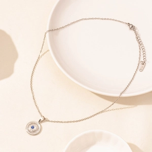 Close-up of silver stainless steel necklace with blue evil eye pendant on a plate