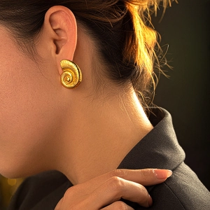 Detailed view of gold conch-shaped textured earring worn on a model's ear