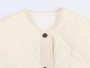 Detailed close-up of beige quilted vest featuring diamond stitching and black buttons