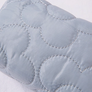 Macro shot of grey-blue quilted fabric with circular patterns and metallic stitching detail
