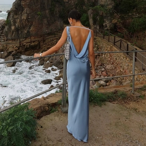 Détail d'une robe longue dos nu en satin bleu sur un fond de côte rocheuse pittoresque