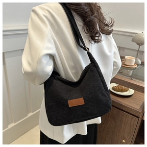 Detail of black corduroy shoulder bag showing brown fashion label and adjustable strap