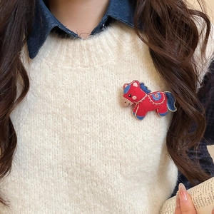 Close-up of a red fabric embroidered pony brooch pinned on a white plush vest