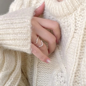 Close-up of minimalist silver wavy ring worn on finger with beige knit sweater background