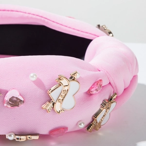 Gros plan d'un serre-tête rose avec strass en cœur, perles et breloque flèche dorée
