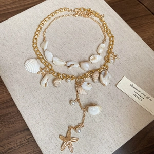 Detail of bohemian layered necklace with golden chain, seashells, and white pearls