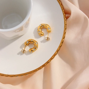 Close-up of golden C-shaped hoop earrings with zircons on a white ceramic tray