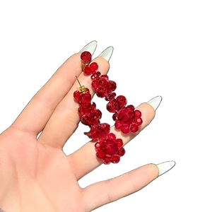 Boucles d'oreilles fleurs en cristal rouge avec tiges dorées tenues à la main élégante