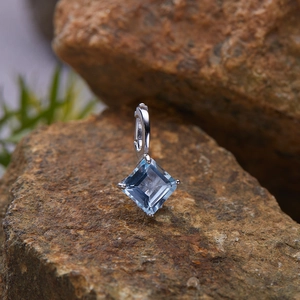 Macro shot of silver pendant with square light blue gemstone on natural rock