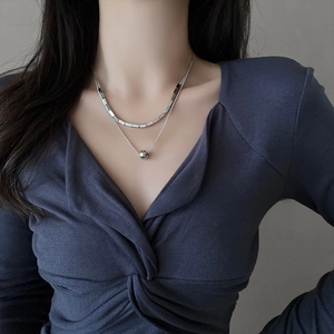 Detail of layered silver necklaces with square beads and a round pendant on a model