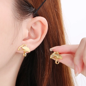 Detail view of gold ginkgo leaf earrings with brushed texture on female model ear