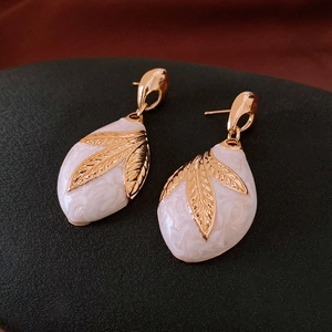 Macro shot of ivory enamel waterdrop earrings with gold leaf-textured metal details