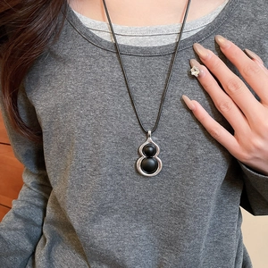 Détail du pendentif gourde en bois avec perles noires mates et cadre argenté sur pull