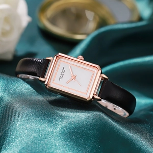 Macro shot of rectangular rose gold quartz watch with black leather strap on green silk