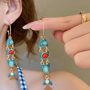 Macro detail of articulating fish drop earrings with vibrant blue enamel and gemstones