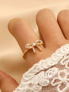 Detailed close-up of a gold bow ring with sparkling zircons against a lace sleeve