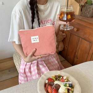 Detailed close-up of pink corduroy makeup bag held by a model in a cozy cafe setting
