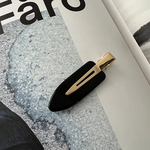 Detailed close-up of a minimalist black acetate hair clip with a polished gold metal clasp
