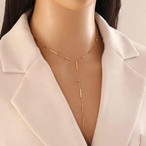 Detail view of a long gold Y-shaped necklace with bar charms and beads on a model