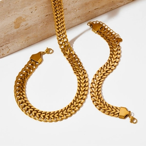 Minimalist golden Cuban link chain necklace and bracelet set on a white stone background