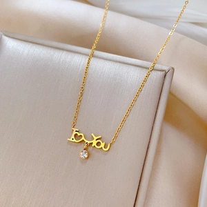 Close-up of golden I love you necklace with zircon pendant on elegant silk background