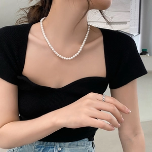 Close-up of a elegant pearl necklace and textured silver ring worn by a model
