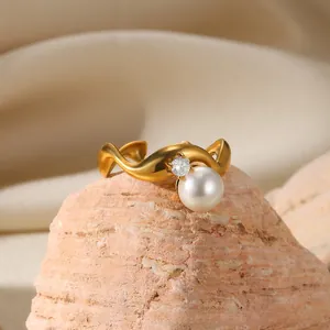 Detail view of gold wave ring with white pearl and diamond on pink textured stone