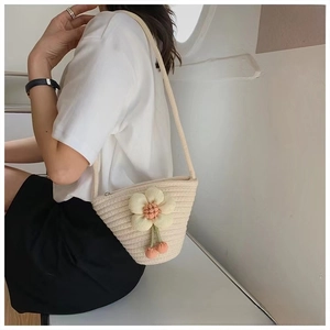 Detail of a beige woven straw shell bag with floral decor and a pink cherry charm