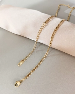 Close-up of golden stainless steel chain necklace with lobster clasp on silk fabric