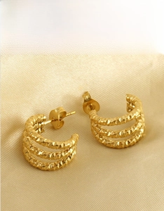 Macro detail of triple-layer gold hoop earrings with hammered metal texture on silk fabric