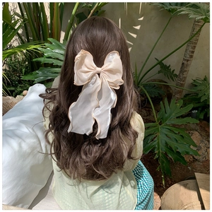 Close-up of a large white mesh bow hair clip styled on a woman's brown wavy hair