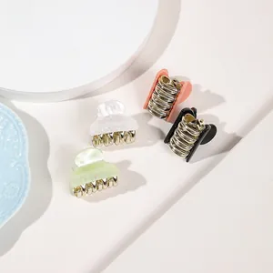 Detail view of four mini acrylic hair claws in assorted colors on a white round display
