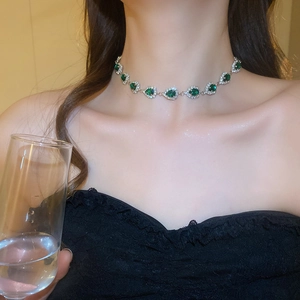 Close-up of a silver necklace with green heart-shaped gemstones on a female model