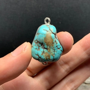 Natural turquoise stone pendant with silver loops and natural matrix veins on dark background