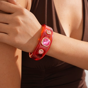 Close-up of a wide red translucent resin bangle with pink rhinestones on a woman's wrist