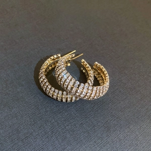 Macro detail of gold C-shape hoop earrings with multiple rows of pavé crystals