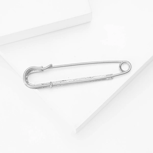 Detailed view of a silver-tone textured rhinestone safety pin brooch on a white platform