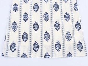 Close-up of white cotton fabric featuring intricate navy blue leaf embroidery patterns