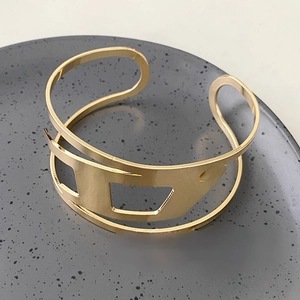 Top view of a gold wide cuff bracelet with geometric hollow cuts on a grey ceramic plate