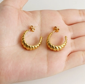 Detailed close-up of 18K gold-plated C-shaped spiral hoop earrings held in hand