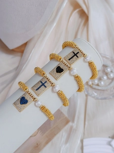 Detail of bohemian gold beaded bracelets featuring enamel crosses and zircon hearts