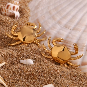 Detailed close-up of 18K gold plated crab earrings on a beach sand and shell backdrop