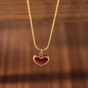 Elegant gold necklace with a red enamel heart pendant on a wooden background