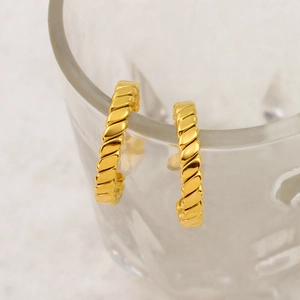 Detailed close-up of golden twisted rope C-shaped hoop earrings on a glass edge