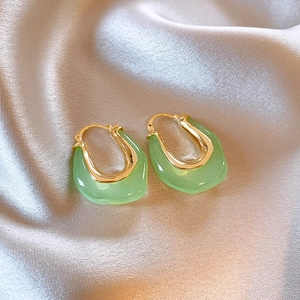 Détail macro de boucles d'oreilles en U dorées avec résine verte sur du tissu