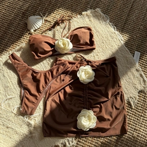 Three-piece brown bikini set with white 3D flower appliqués on top and drawstring skirt