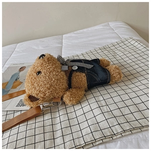 Detail of plush dog phone bag in denim overalls sitting on checkered fabric